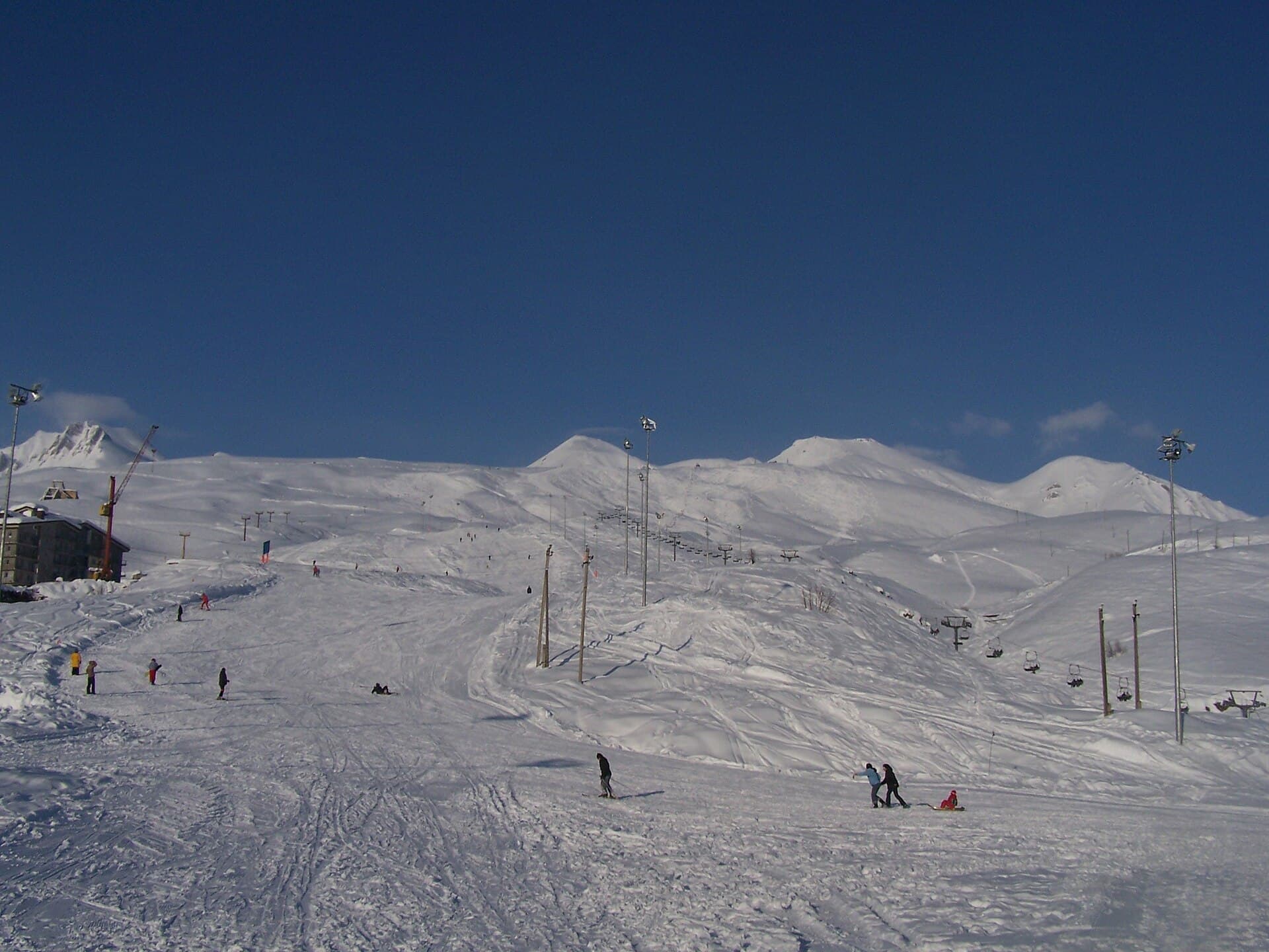 Skiers and sledders on wide snow-covered slopes at Gudauri resort under a deep blue sky