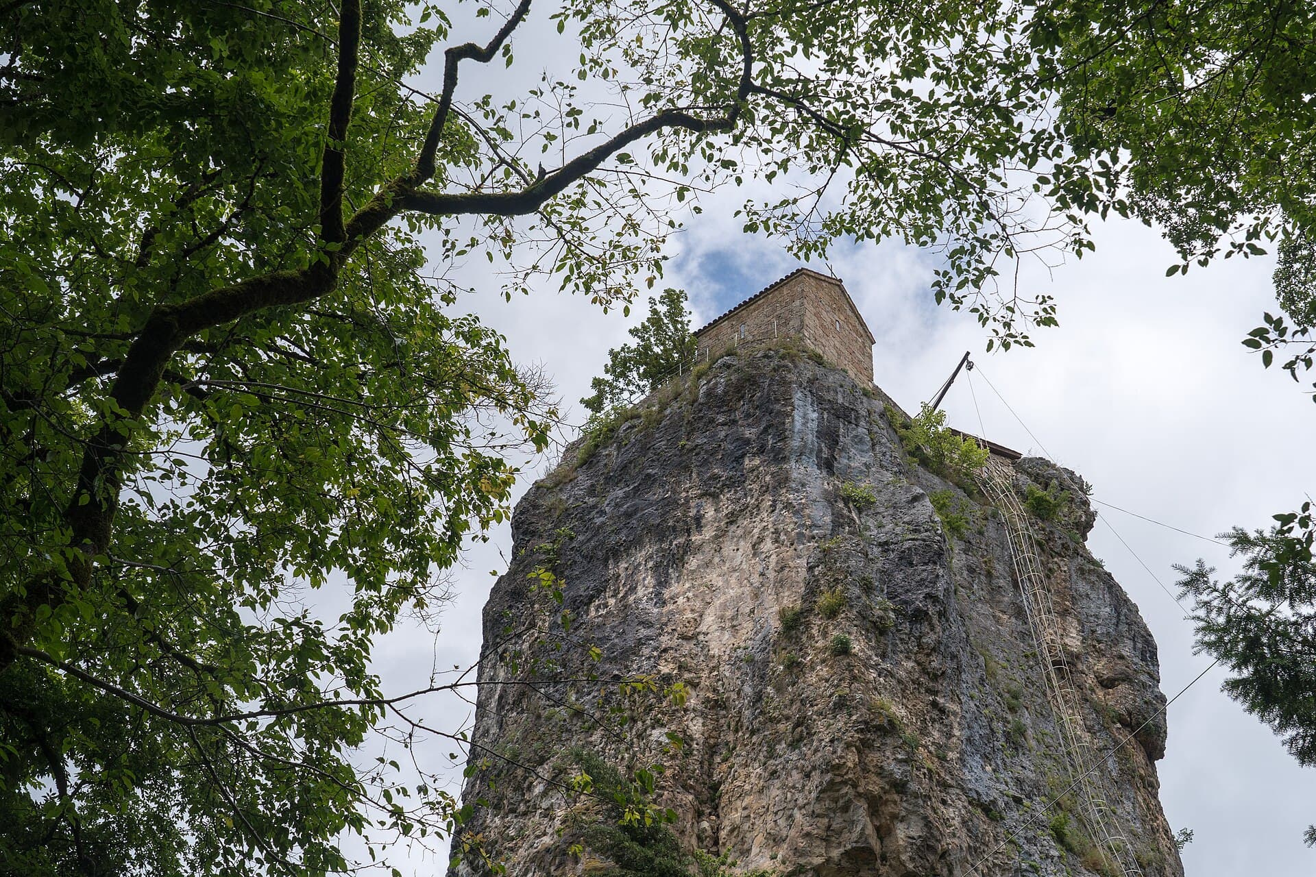 The Katskhi Pillar — a lone limestone monolith topped by a small monastery, seen through trees