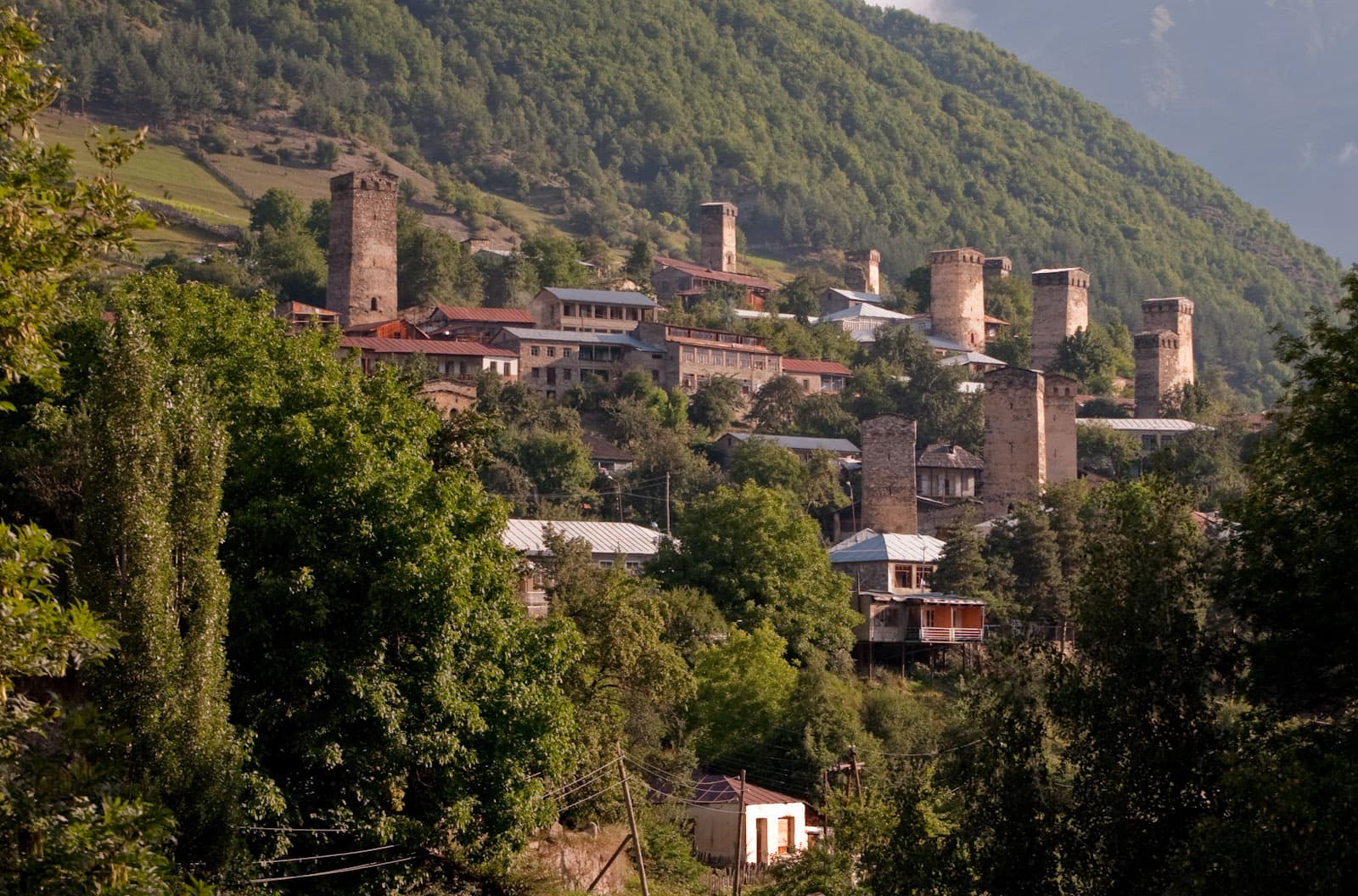 Stone Svan towers rising between trees and houses in Mestia at golden hour