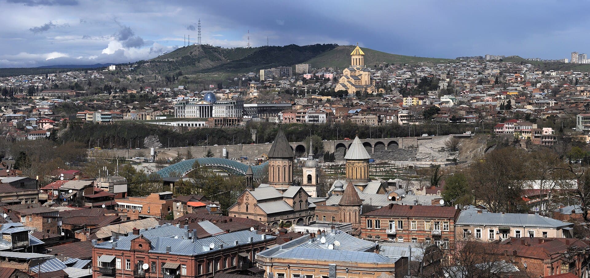 Panoramic view over Tbilisi’s old-town rooftops and churches, with Sameba Cathedral on the hill behind